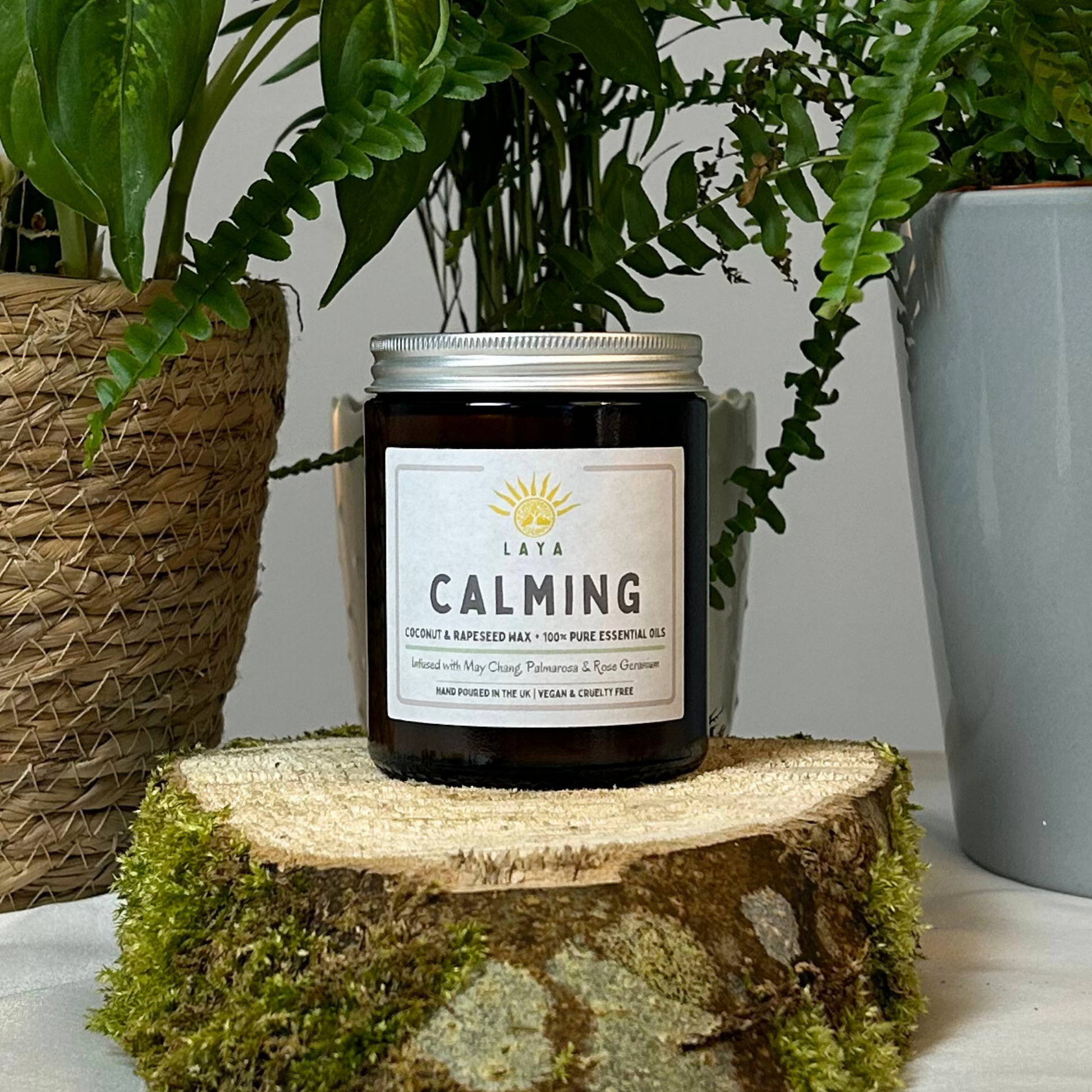 Natural calming candle by Laya in amber glass jar, displayed on wood & set against peaceful backdrop.