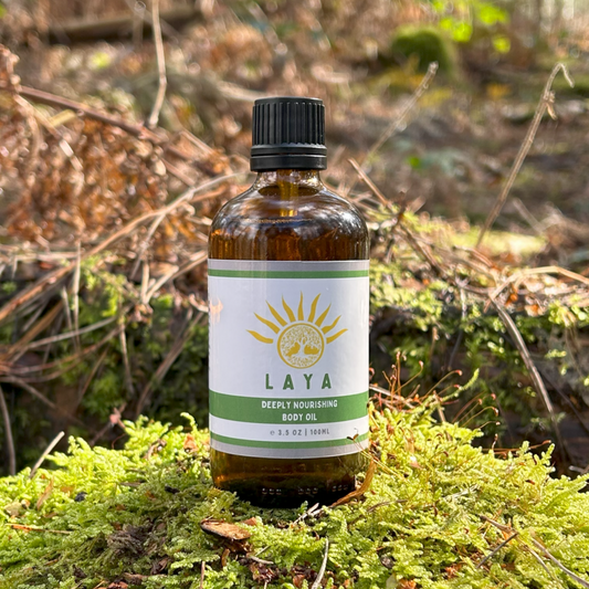 Deeply Nourishing Body Oil by Laya, displayed outdoors on leafy tree stump in a close-up view.