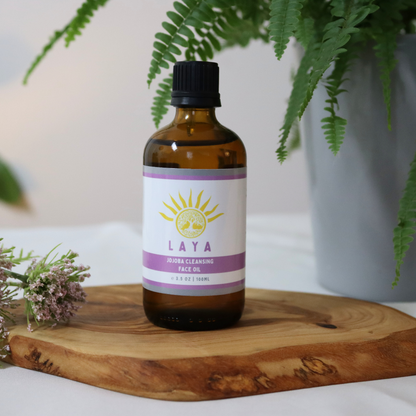 Jojoba Cleansing Face Oil by Laya, displayed on wood next to plant and purple flower.