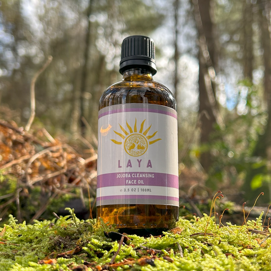 Close-up of Laya's Jojoba Cleansing Face Oil outdoors, on leafy green tree stump.