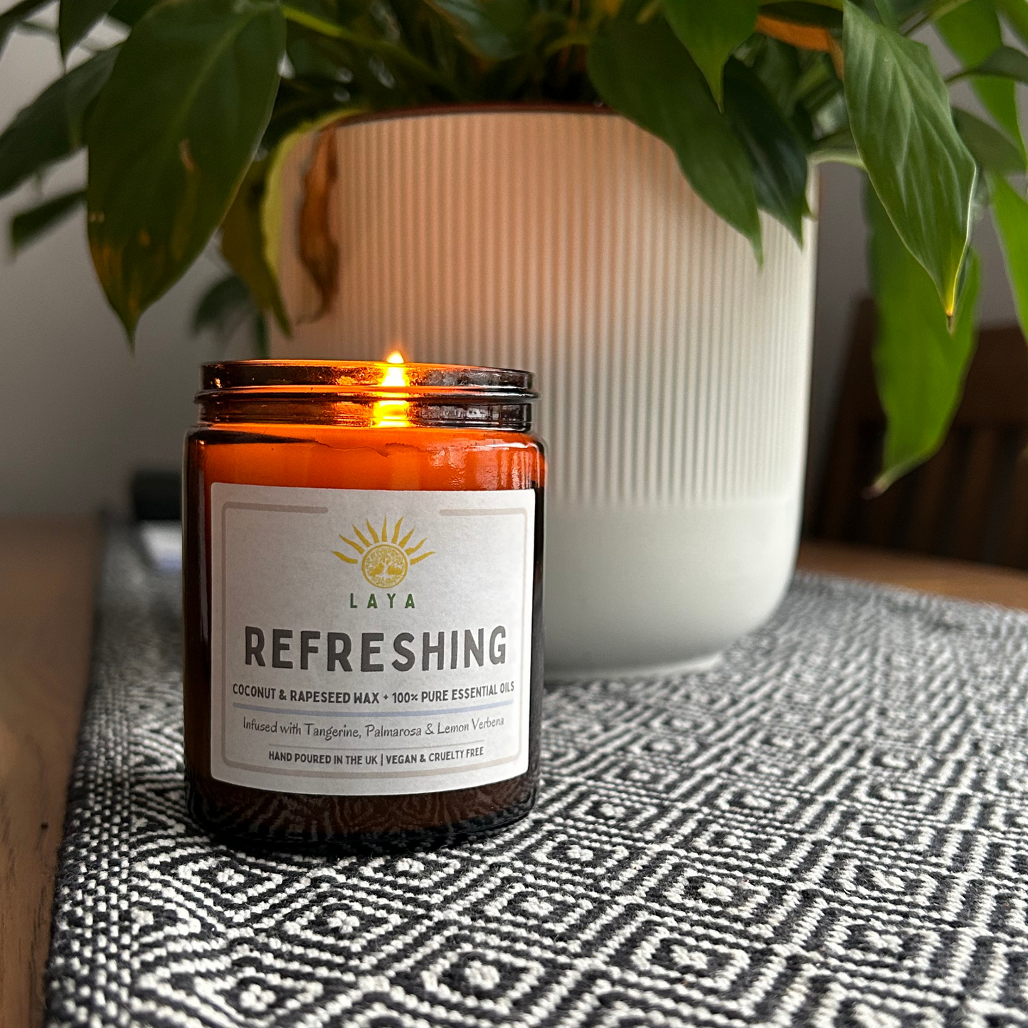 Lit refreshing coconut and rapeseed candle by Laya, gently flickering on a side table in a peaceful setting.