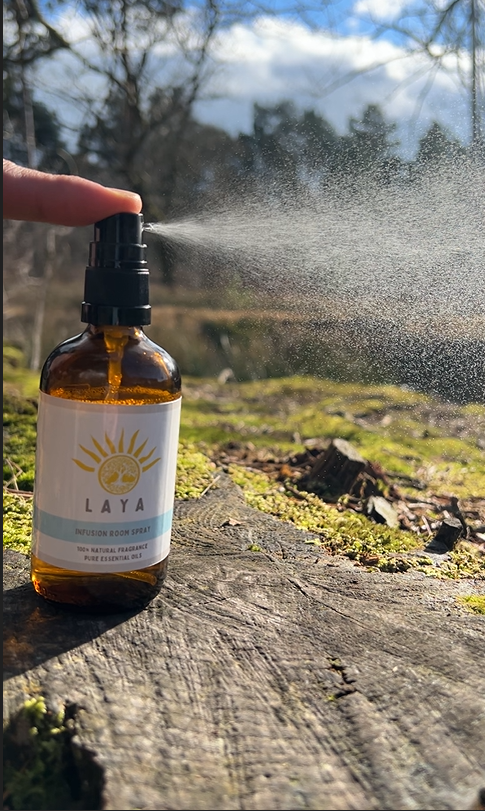 Laya's 100ml room spray releasing a fine mist outdoors, displayed outdoors next to a lake.